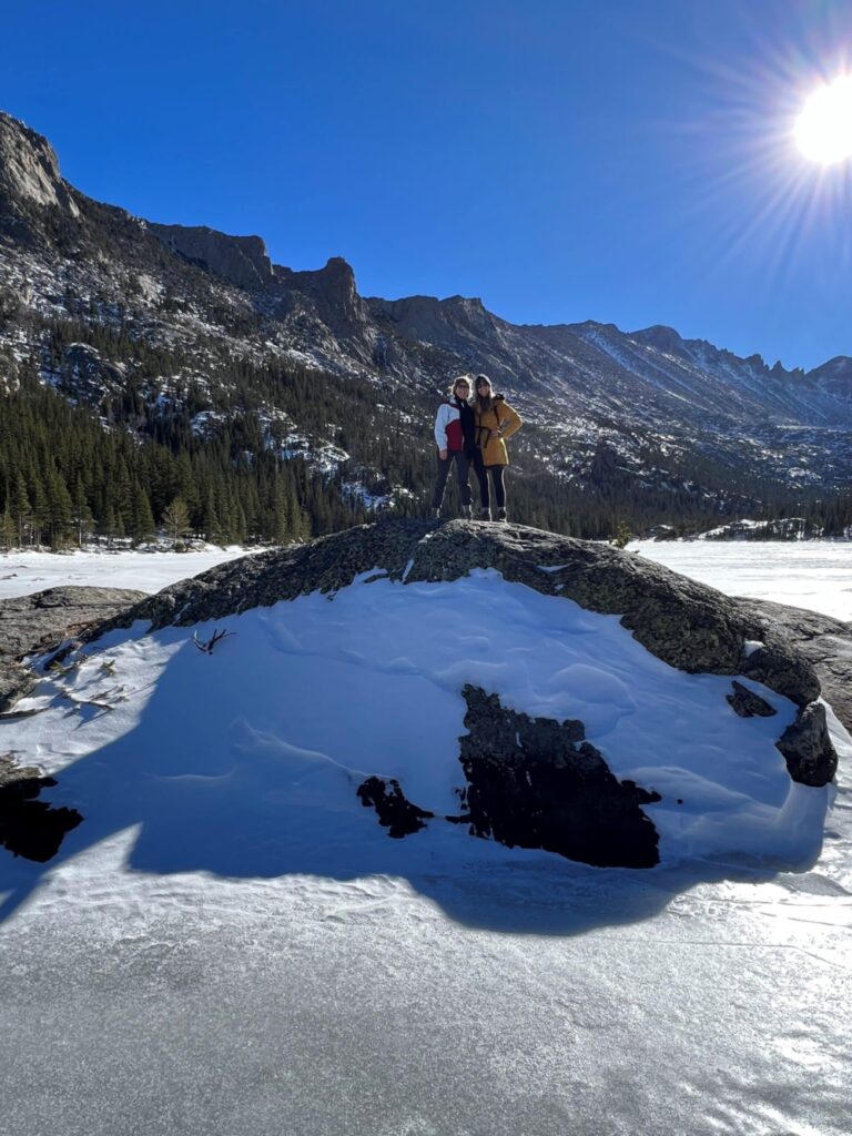 Two women standing on a rock in the middle of a frozen lake.