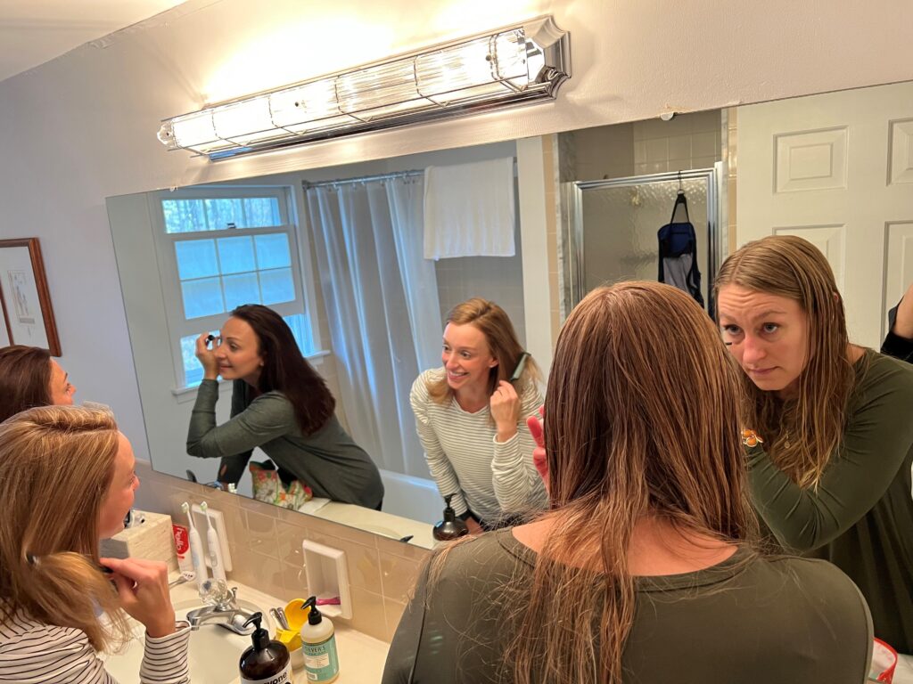 Three young women in the mirror together getting ready to go out.