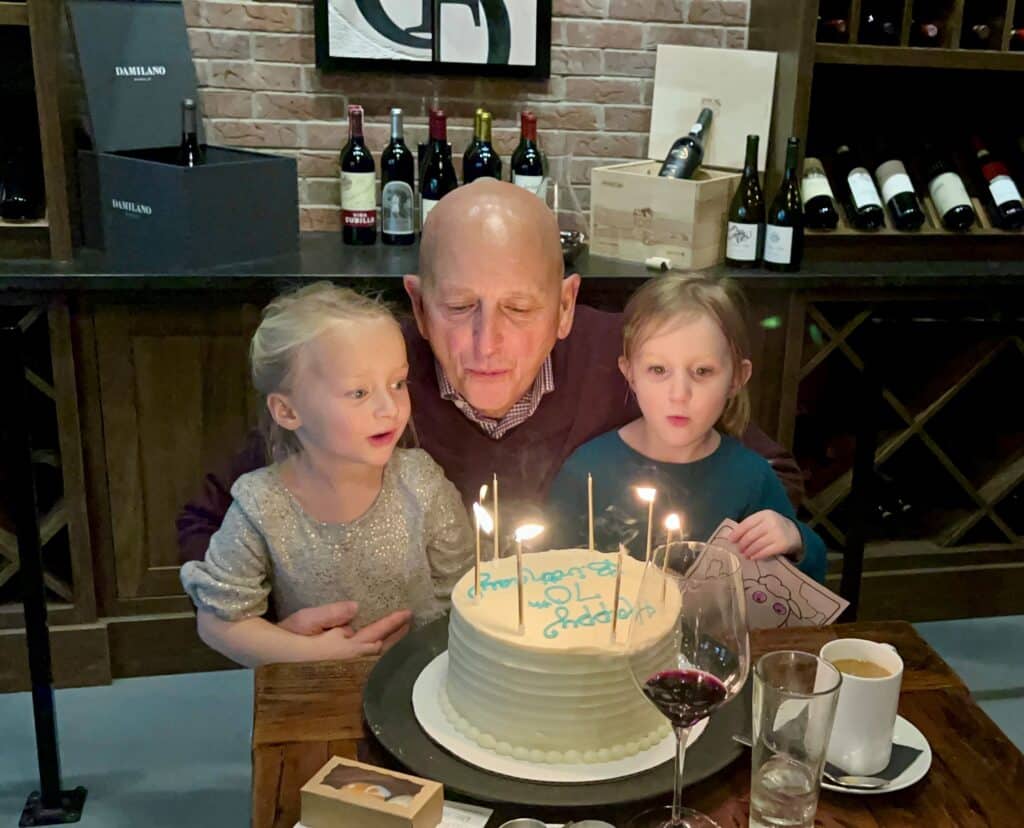 Granddaughters help Grandpa blow out his birthday candles.