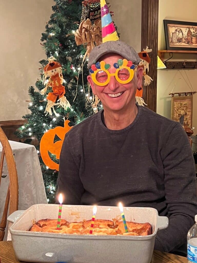 Man with birthday hat and silly glasses with birthday cake and candles.