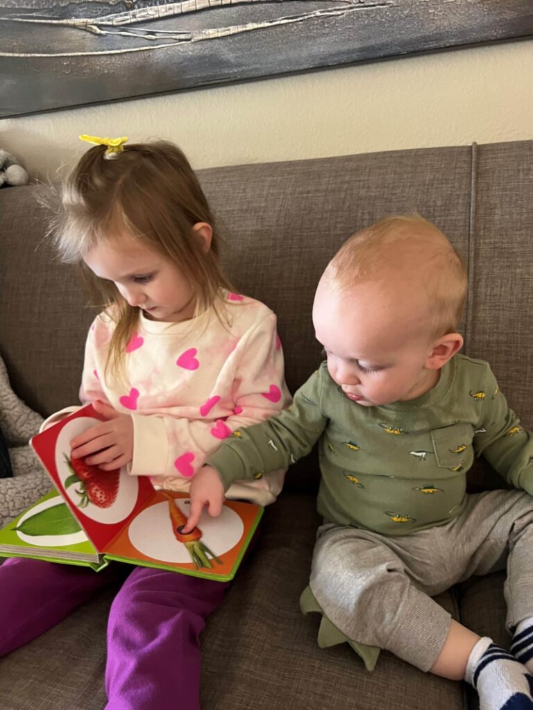 A 4-year-old and her 1-year-old brother reading a book together. 