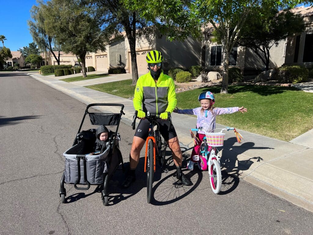 A Papa and his granddaughter on bikes with baby brother in wagon stroller.