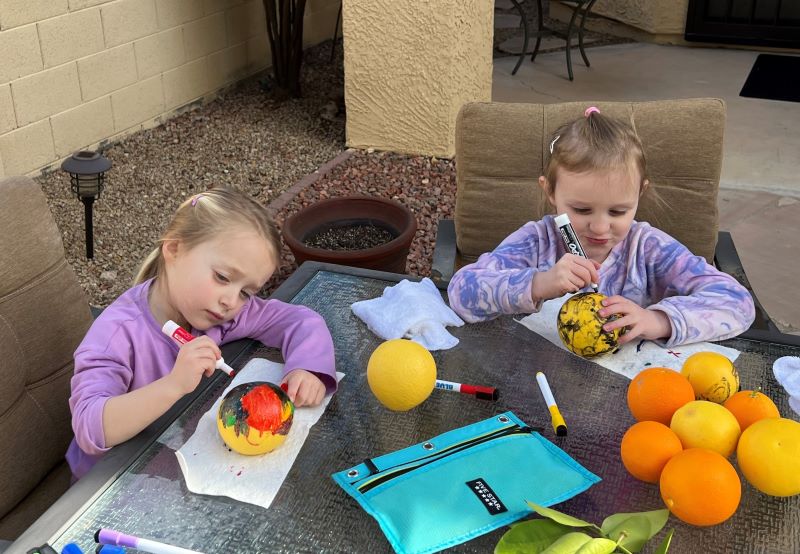 Two little girls coloring on grapefruits they picked from Nana's tree in Phoenix.