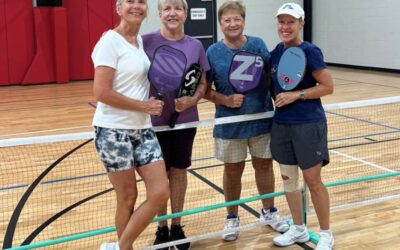 4 women posing with pickleball paddles