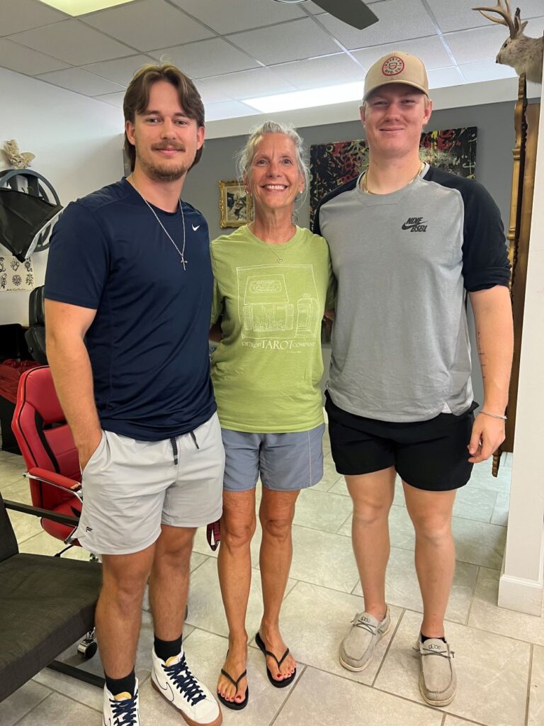 An woman poses for a photo with two young men at a tattoo parlor as they are all their to get new tattoos.